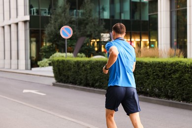 Photo of Man in sportswear running outdoors, back view