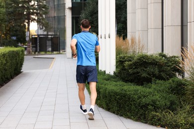 Photo of Man in sportswear running outdoors, back view