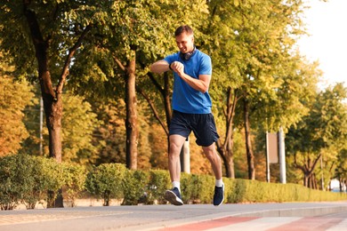 Photo of Man checking fitness tracker while running outdoors