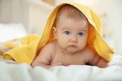 Photo of Cute baby covering with yellow towel after bathing on bed, closeup