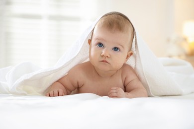 Photo of Cute baby covering with towel after bathing on bed, closeup