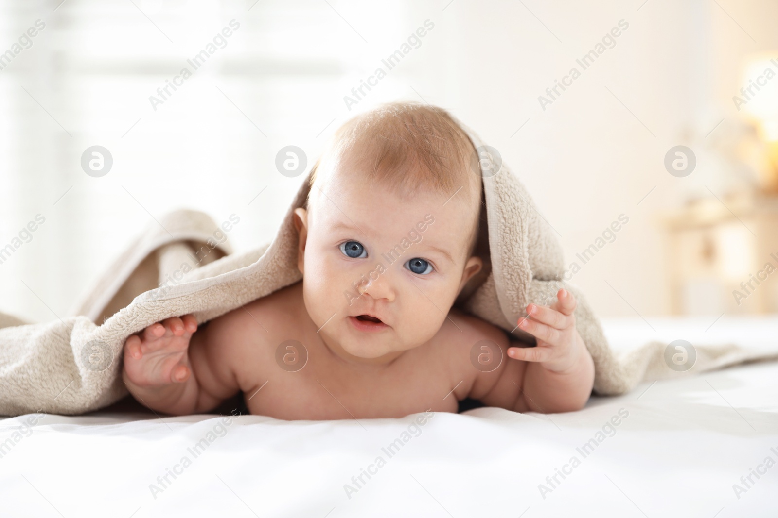 Photo of Cute baby covering with beige towel after bathing on bed, closeup