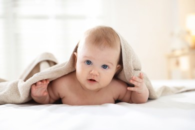 Photo of Cute baby covering with beige towel after bathing on bed, closeup