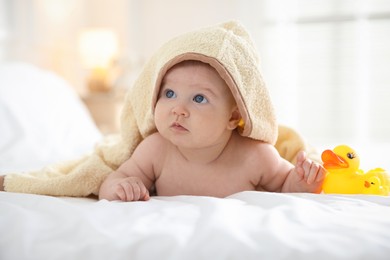 Photo of Cute baby covering with yellow towel with rubber ducks after bathing on bed, closeup