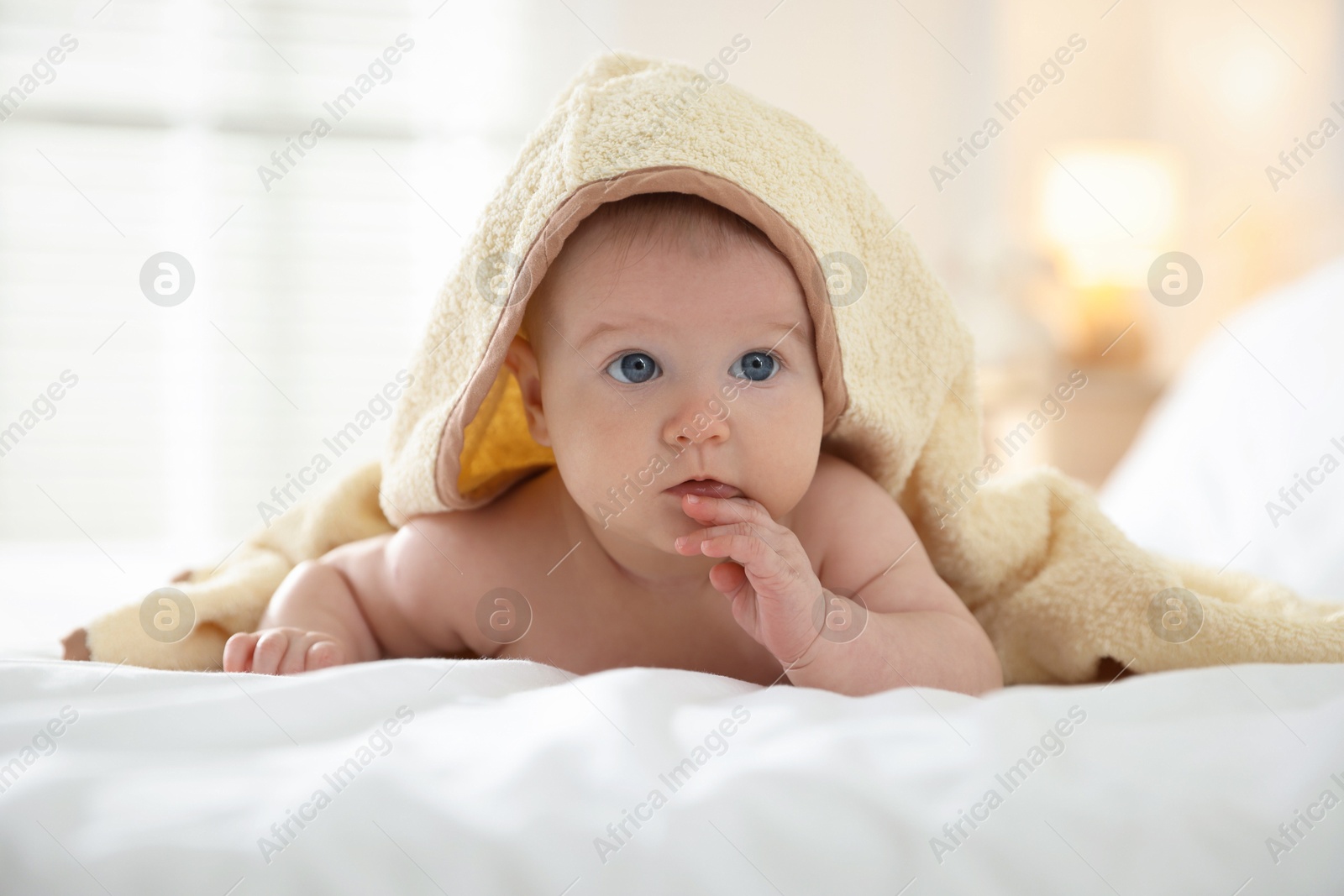Photo of Cute baby covering with yellow towel after bathing on bed, closeup