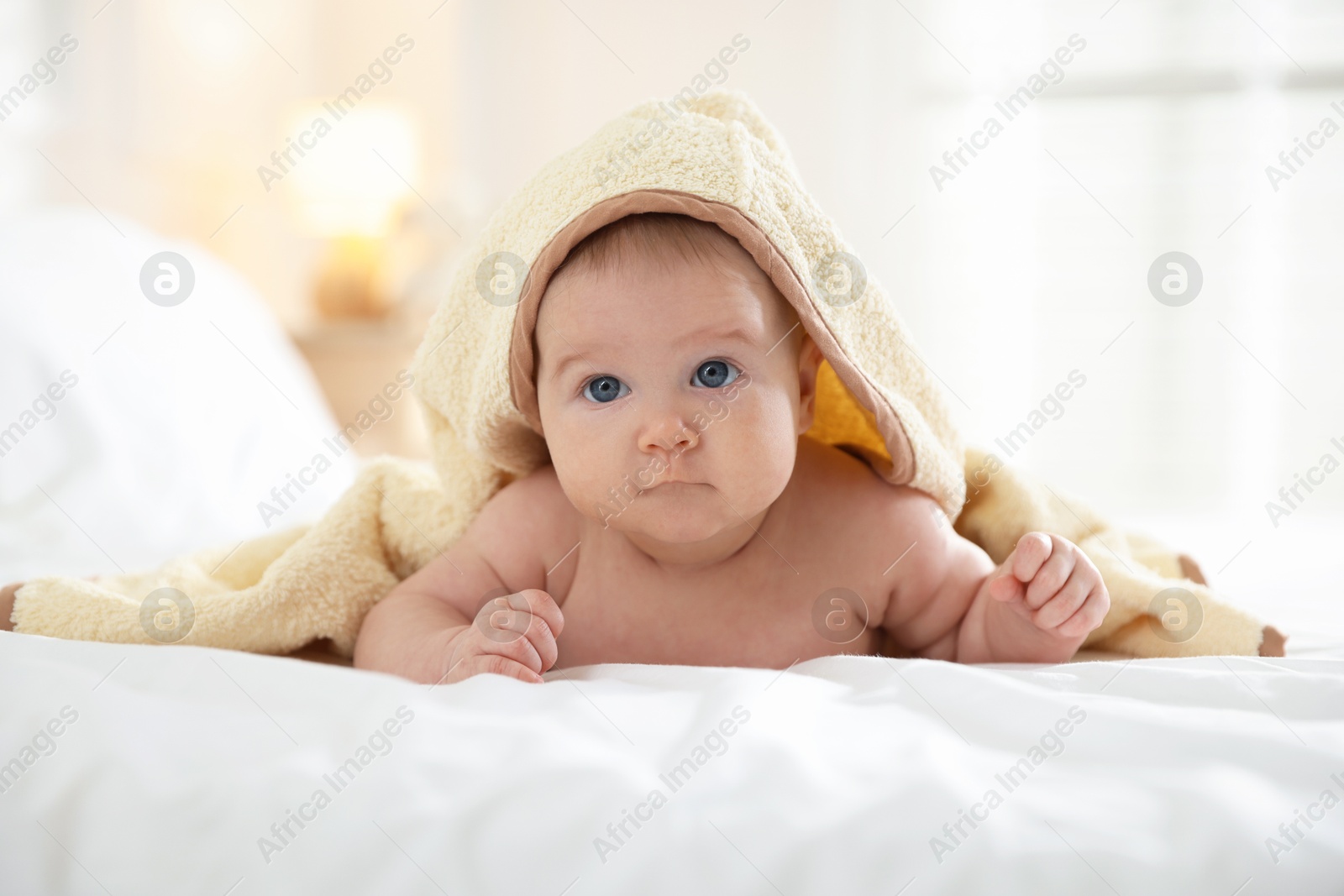 Photo of Cute baby covering with yellow towel after bathing on bed, closeup