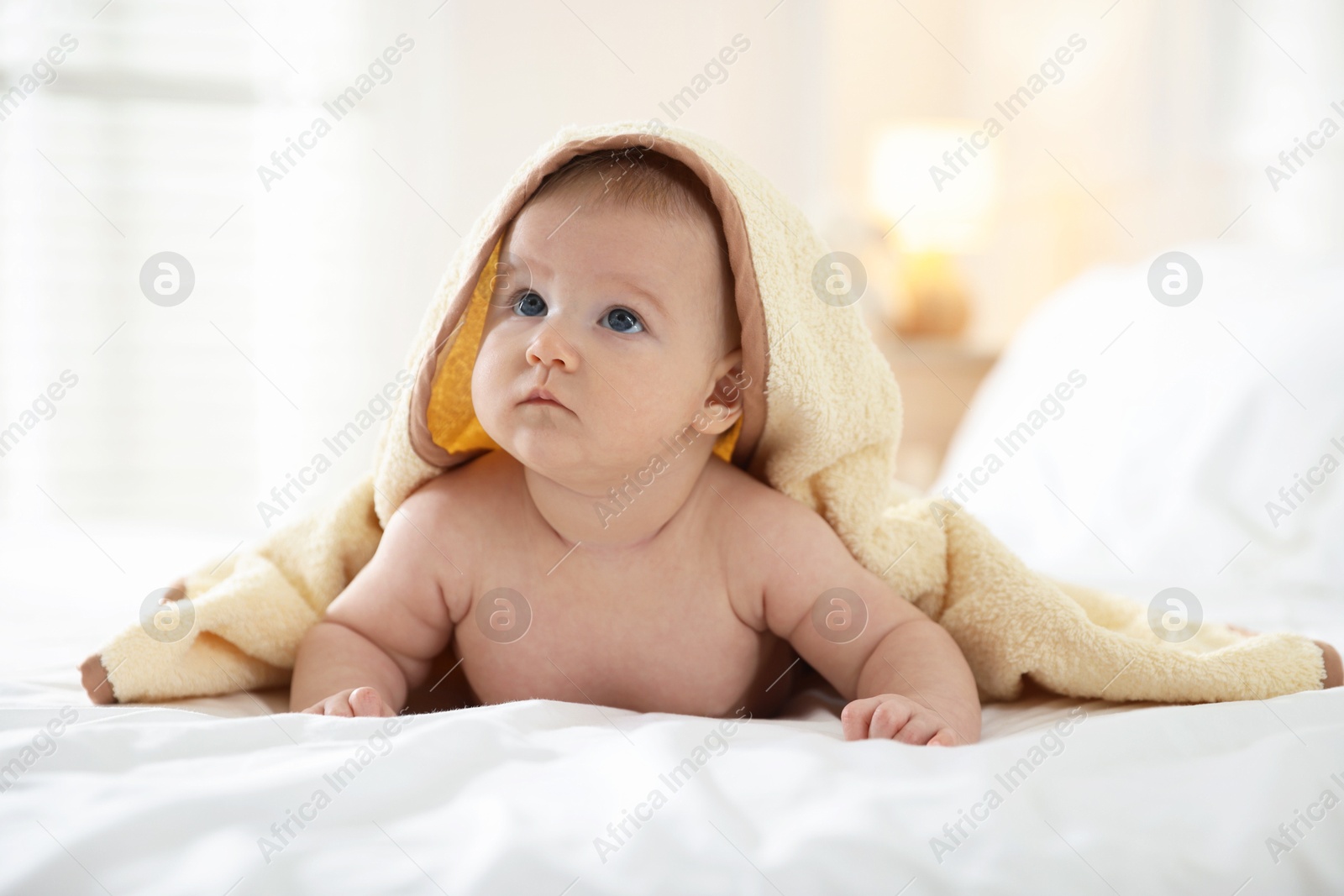 Photo of Cute baby covering with yellow towel after bathing on bed, closeup