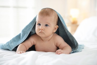 Photo of Cute baby covering with blue towel after bathing on bed, closeup