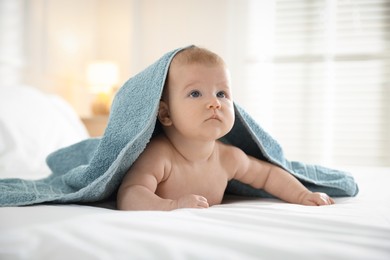 Photo of Cute baby covering with blue towel after bathing on bed, closeup