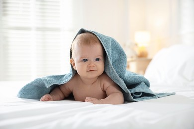 Photo of Cute baby covering with blue towel after bathing on bed, closeup
