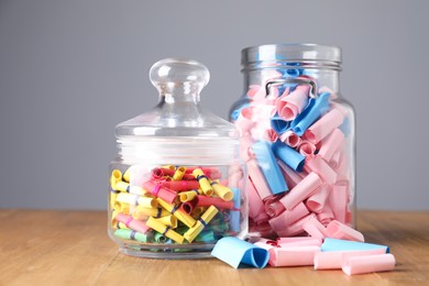 Photo of Colorful paper notes in glass jars on wooden table against grey background