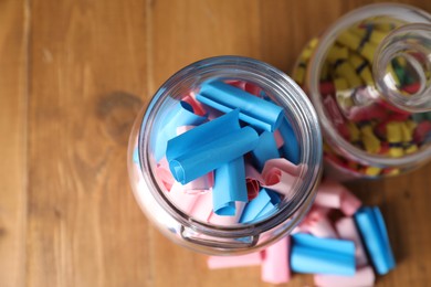 Photo of Colorful paper notes in glass jars on wooden table, flat lay. Space for text