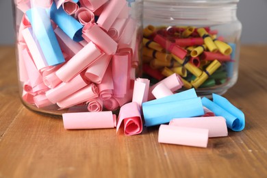 Photo of Colorful paper notes in glass jars on wooden table, closeup
