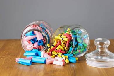 Photo of Colorful paper notes in glass jars on wooden table against grey background