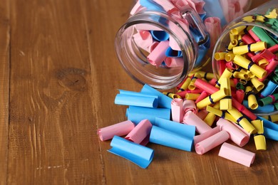 Photo of Colorful paper notes in glass jars on wooden table, closeup. Space for text