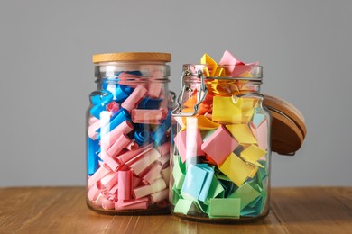 Photo of Colorful paper notes in glass jars on wooden table against grey background