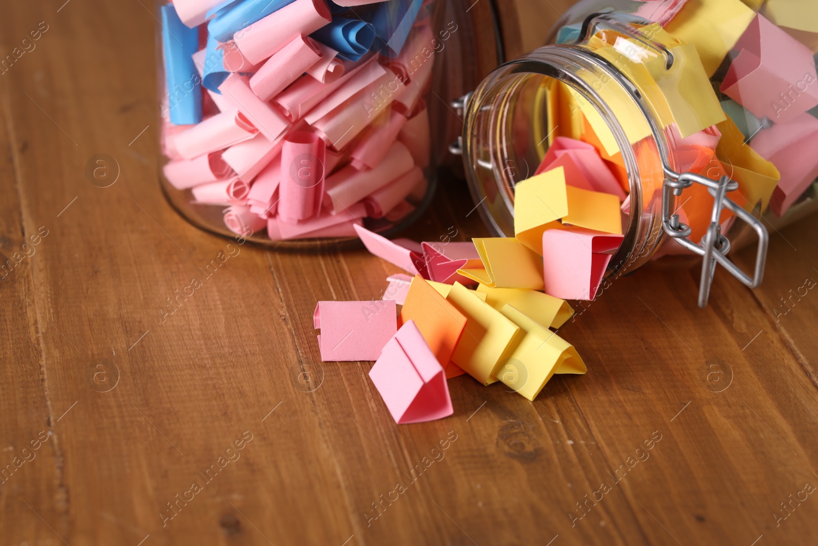 Photo of Colorful paper notes in glass jars on wooden table, closeup. Space for text