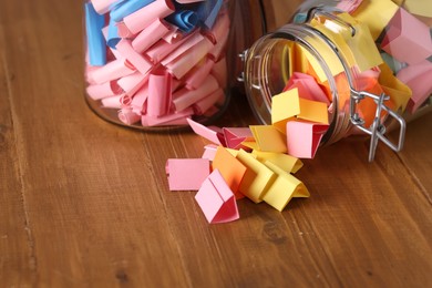 Photo of Colorful paper notes in glass jars on wooden table, closeup. Space for text