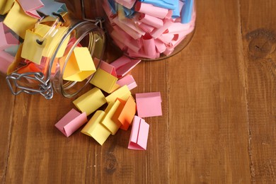 Photo of Colorful paper notes in glass jars on wooden table, above view. Space for text