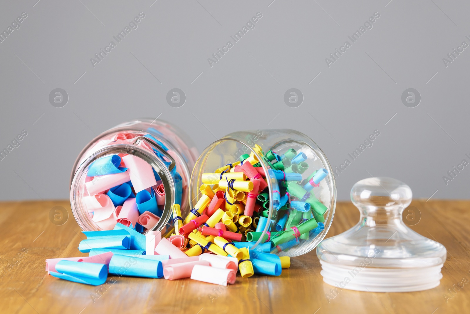 Photo of Colorful paper notes in glass jars on wooden table against grey background, closeup
