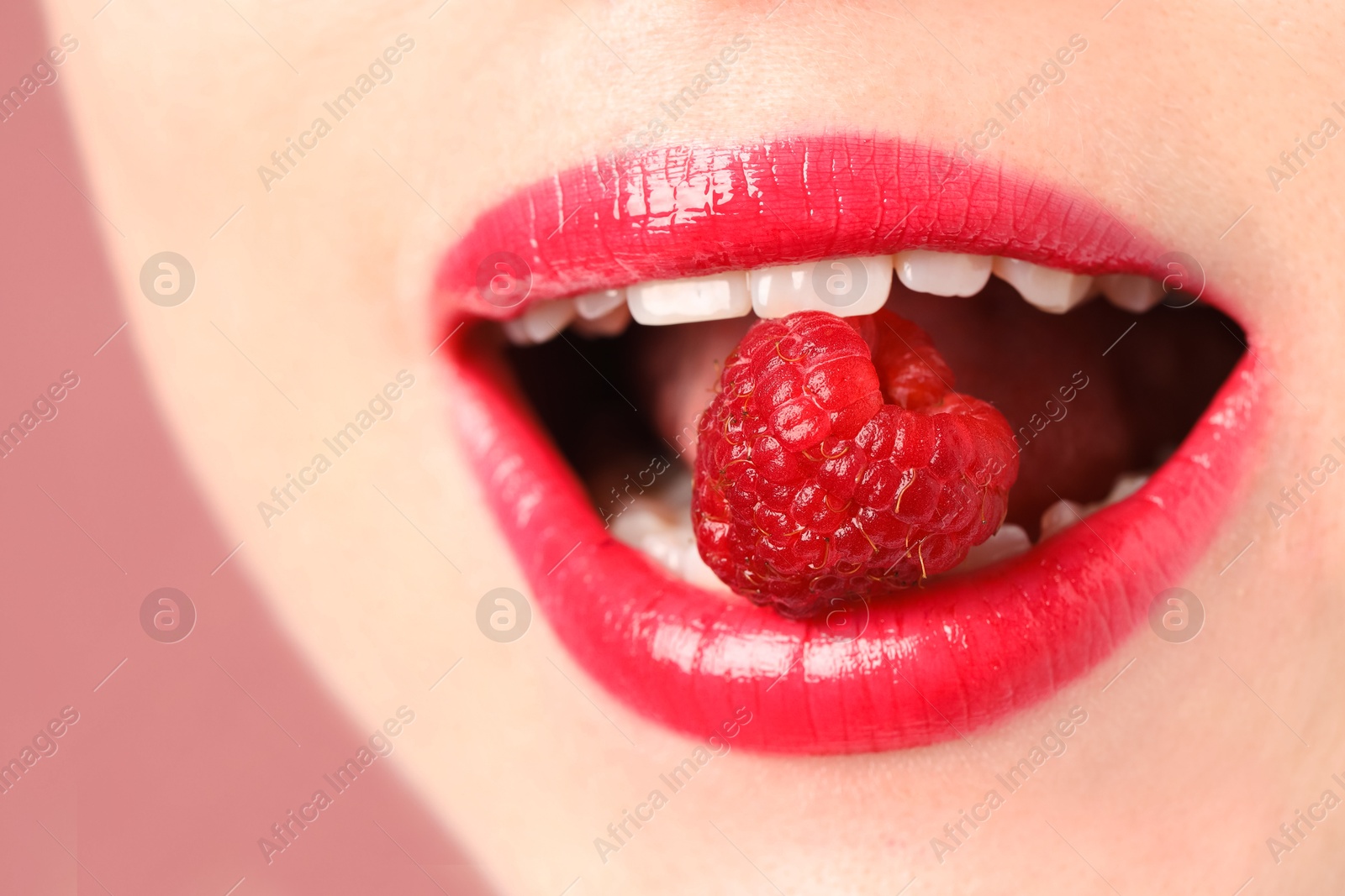 Woman with beautiful lips makeup and raspberry on dusty pink background, closeup Photo of Woman with beautiful lips makeup and raspberry on dusty pink background, closeup