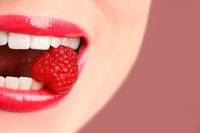 Photo of Woman with beautiful lips makeup and raspberry on dusty pink background, closeup. Space for text