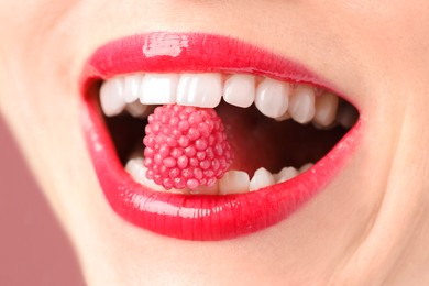 Photo of Woman with beautiful lips makeup and raspberry candy on dusty pink background, closeup