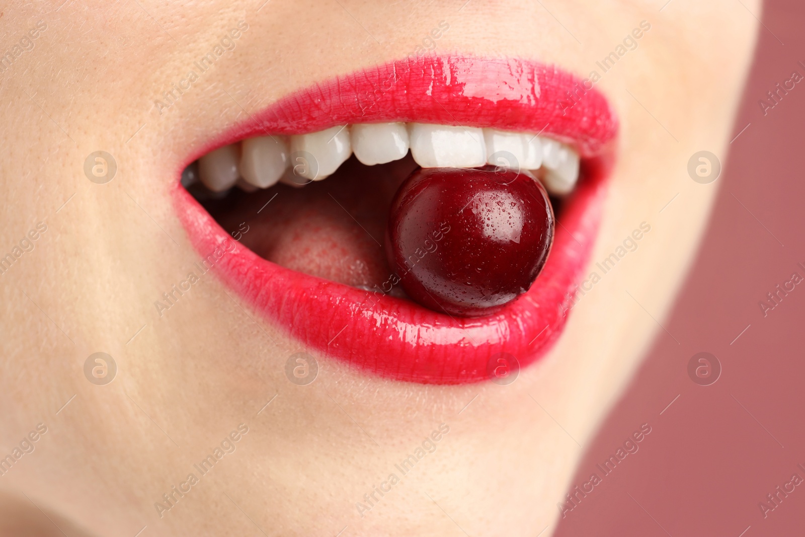 Photo of Woman with beautiful lips makeup and cherry on dusty pink background, closeup