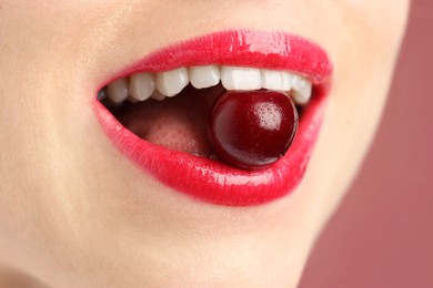 Photo of Woman with beautiful lips makeup and cherry on dusty pink background, closeup
