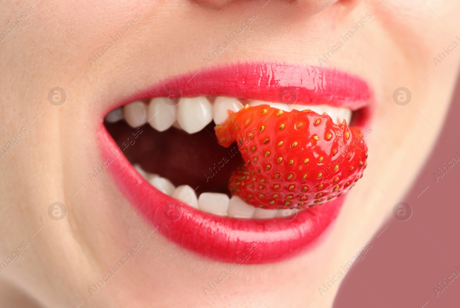 Woman with beautiful lips makeup and strawberry on dusty pink background, closeup Photo of Woman with beautiful lips makeup and strawberry on dusty pink background, closeup