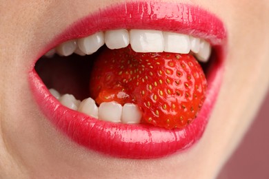 Photo of Woman with beautiful lips makeup and strawberry on dusty pink background, closeup