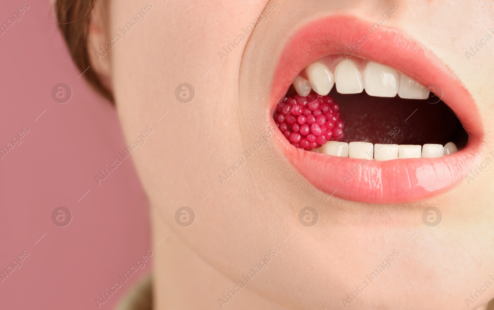 Woman with beautiful lips makeup and raspberry candy on dusty pink background, closeup Photo of Woman with beautiful lips makeup and raspberry candy on dusty pink background, closeup
