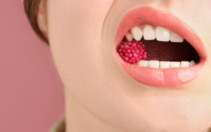 Photo of Woman with beautiful lips makeup and raspberry candy on dusty pink background, closeup