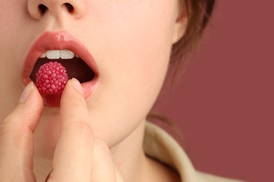 Photo of Woman with beautiful lips makeup and raspberry candy on dusty pink background, closeup. Space for text