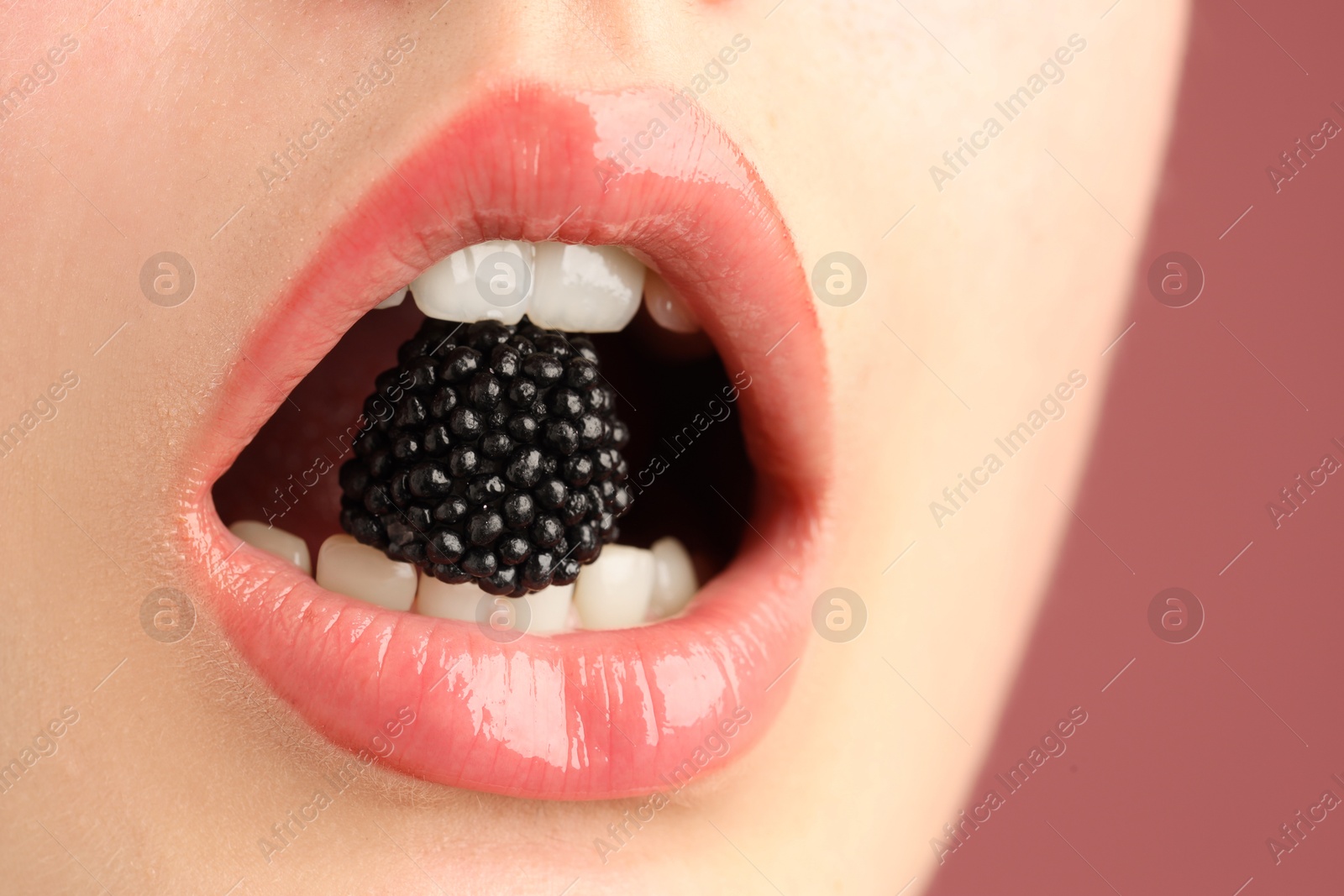 Woman with beautiful lips makeup and blackberry on dusty pink background, closeup Photo of Woman with beautiful lips makeup and blackberry on dusty pink background, closeup