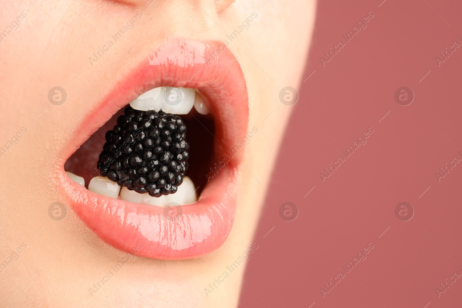 Photo of Woman with beautiful lips makeup and blackberry on dusty pink background, closeup. Space for text