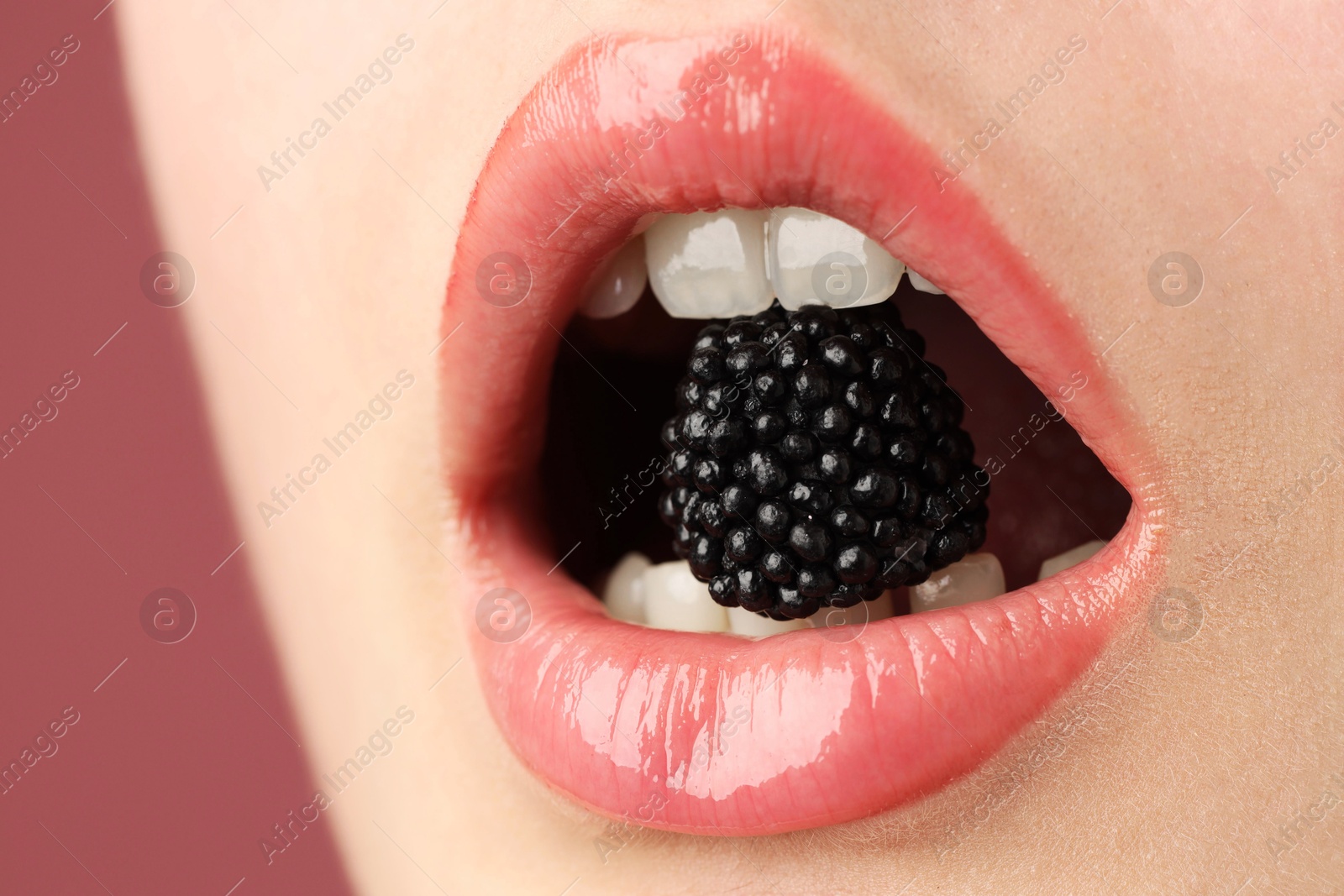 Photo of Woman with beautiful lips makeup and blackberry on dusty pink background, closeup