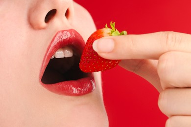 Photo of Woman with beautiful lips makeup and strawberry on red background, closeup