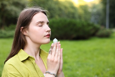 Photo of Woman meditating with crystal to heal or restore her aura outdoors, space for text