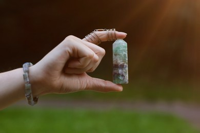 Photo of Woman meditating with crystal to heal or restore her aura outdoors, closeup