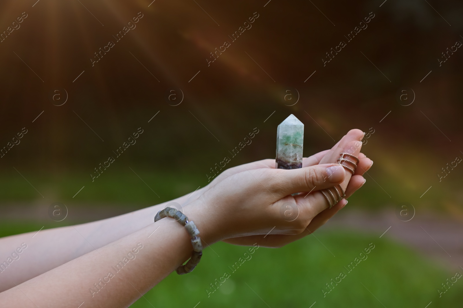 Photo of Woman meditating with crystal to heal or restore her aura outdoors, closeup