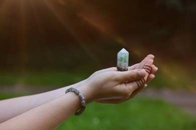 Photo of Woman meditating with crystal to heal or restore her aura outdoors, closeup