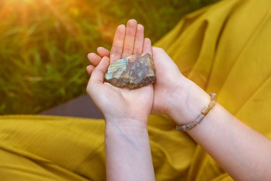 Photo of Woman meditating with crystal to heal or restore her aura outdoors, closeup