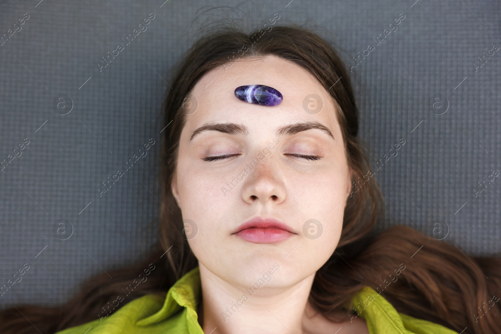 Photo of Woman meditating with crystal to heal or restore her aura on mat, above view