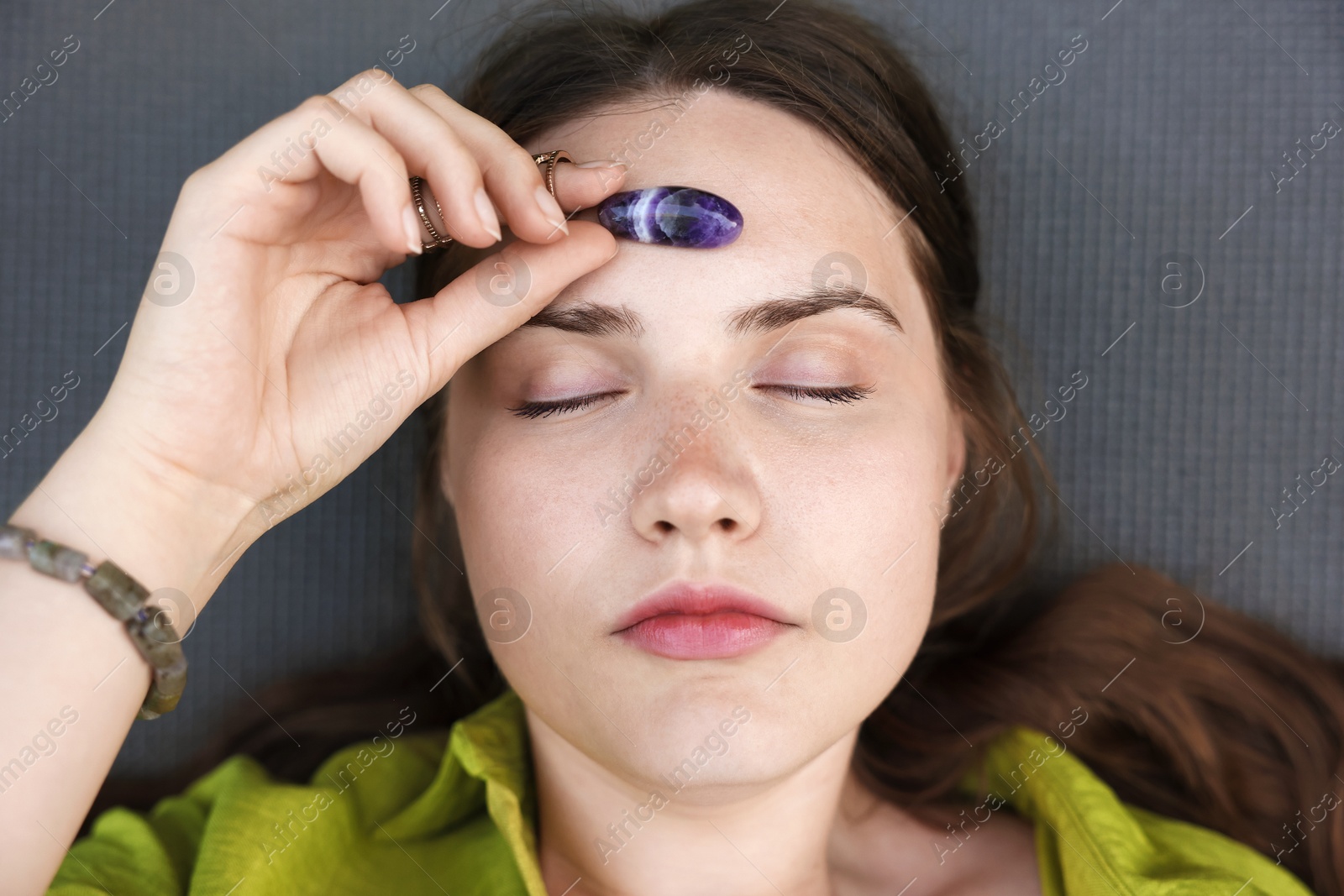 Photo of Woman meditating with crystal to heal or restore her aura on mat, above view