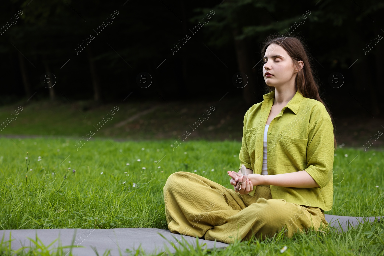 Photo of Woman meditating with crystal to heal or restore her aura outdoors, space for text