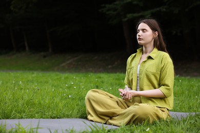 Photo of Woman meditating with crystal to heal or restore her aura outdoors, space for text
