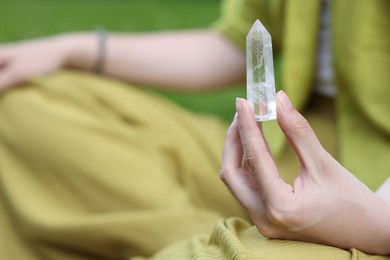 Photo of Woman meditating with crystal to heal or restore her aura outdoors, closeup