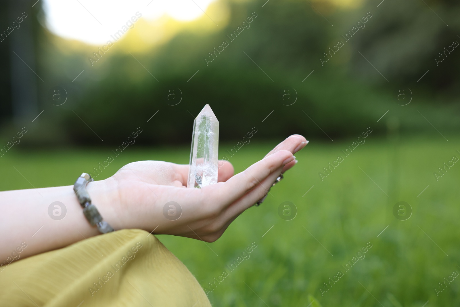 Photo of Woman meditating with crystal to heal or restore her aura outdoors, closeup
