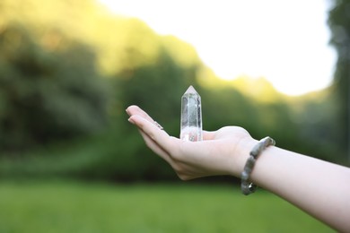 Photo of Woman meditating with crystal to heal or restore her aura outdoors, closeup
